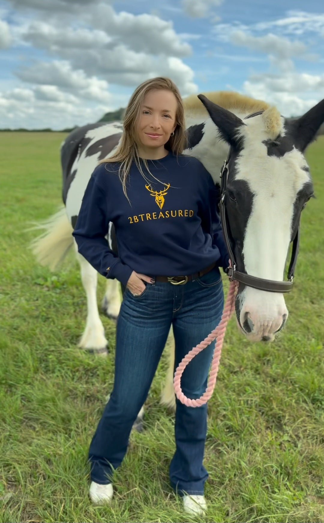 Female model wearing the Embroidered Harris Sweatshirt with gold branding next to a horse in field