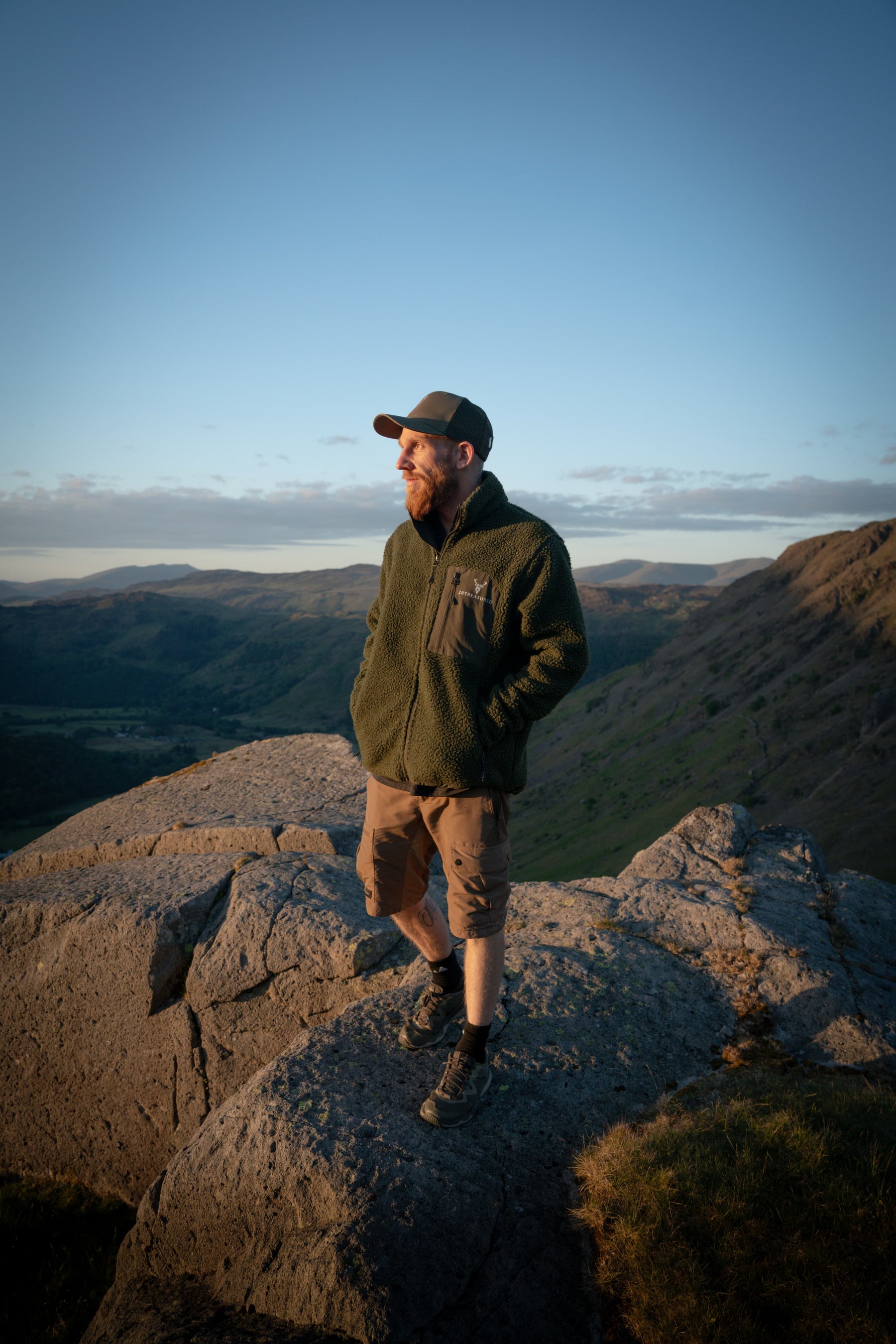 Man modelling fleece on top of a mountain with hill landscape in background