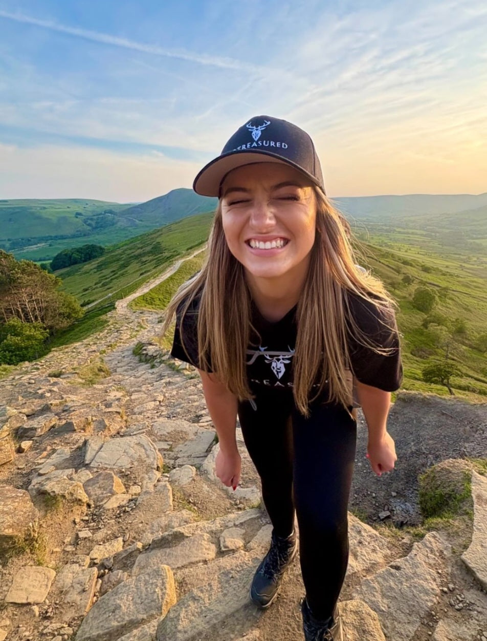 Female model wearing black 2BTreasured hat and tshirt on top of a hill smiling