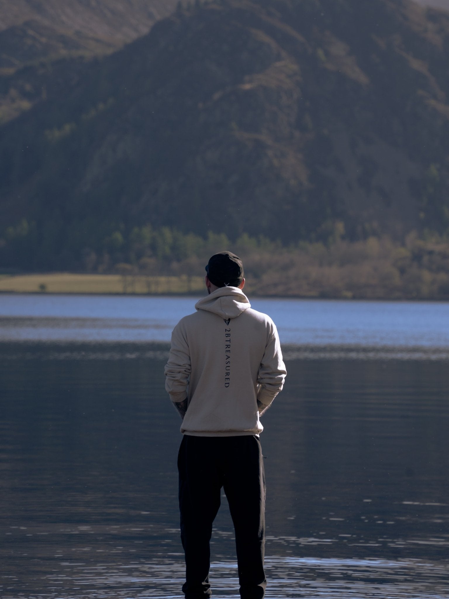 Embroidered Glen Etive Hoodie with British Flag worn by male model standing next to the water will hills in the background