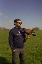 Male wearing the Embroidered Harris Sweatshirt in navy colour from 2BTreasured holding a hawk in field 