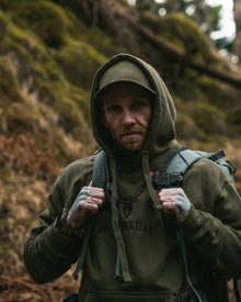 Male model wearing Embroidered Lomond Hoodie with British Flag on sleeve in Military Green from clothing brand 2BTreasured in a forest setting 