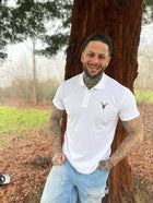 Embroidered Premium Hillside Polo Shirt in white worn by a man in woodlands