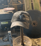 Embroidered Stag Camouflage Trucker Hat olive camo featured on a stick in a barn