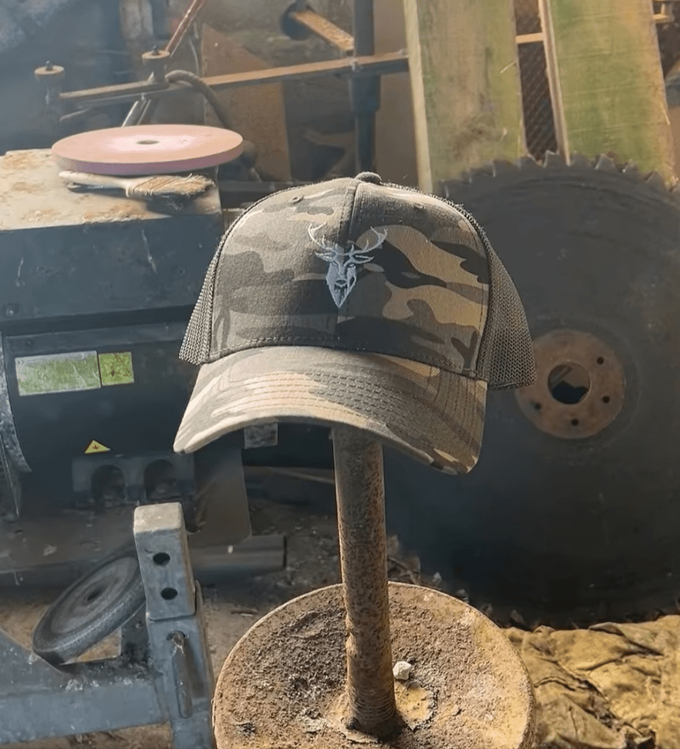 Embroidered Stag Camouflage Trucker Hat olive camo featured on a stick in a barn