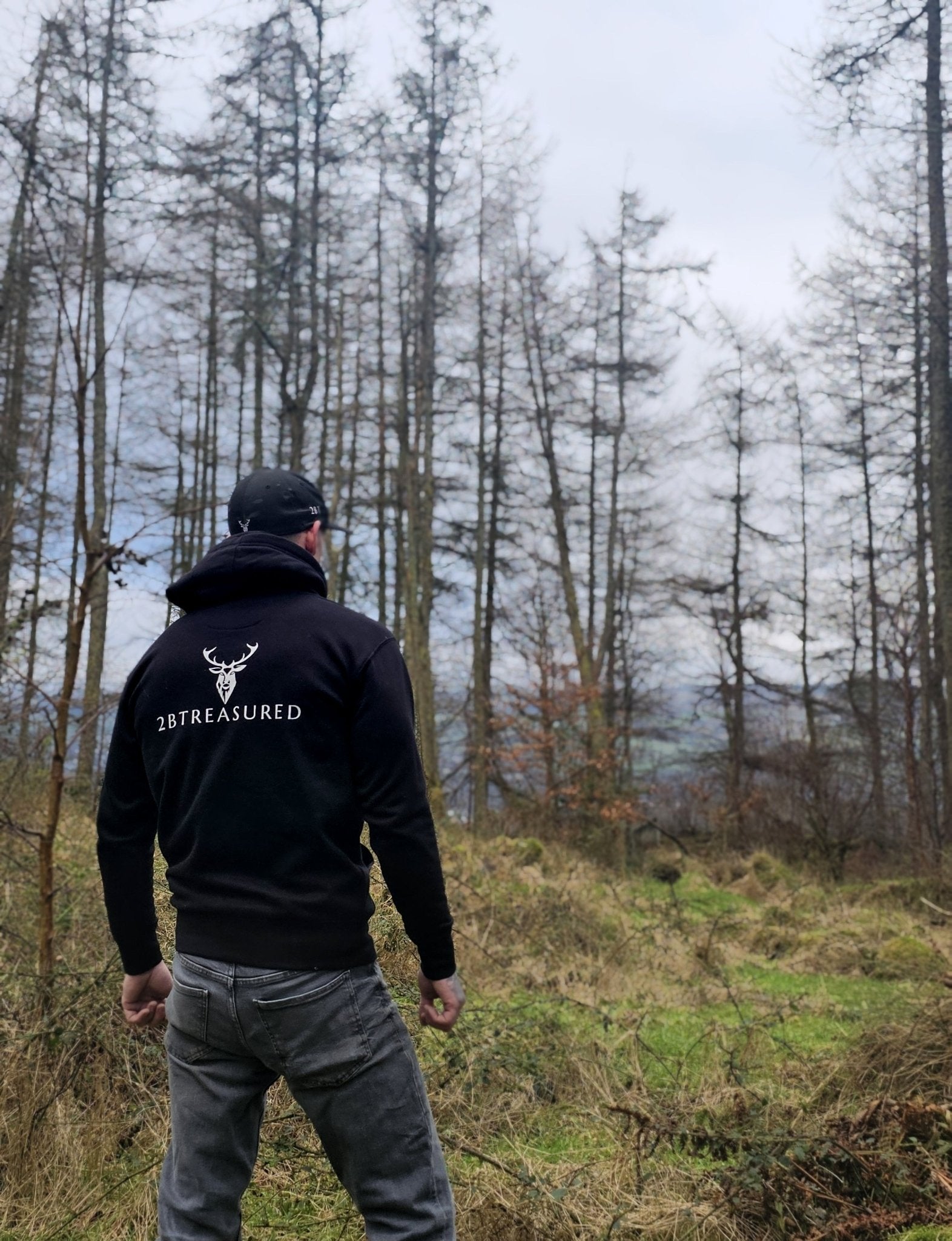 Embroidered Stag Lomond Hoodie in Black worn by male model in a forest back view