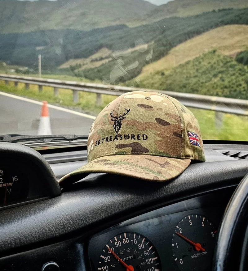 Embroidered Structured Camo Cap with British Flag Multicam Green on top of car dashboard with hills in background