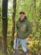 Mdoel is wearing Snowdon Sherpa Fleece Army Green and camo cap standing in a woodland