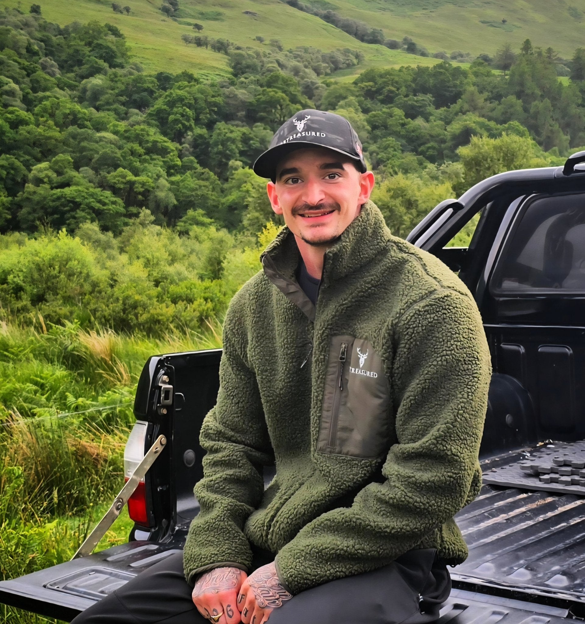 Male model wearing Snowdon Sherpa Fleece Army Green colour from brand 2BTreasured on the back of a truck in the countryside 